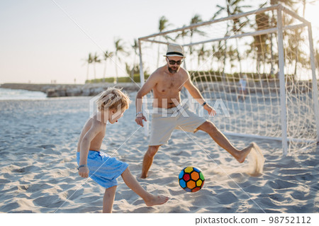 Father with his son plaing football on the beach. 98752112