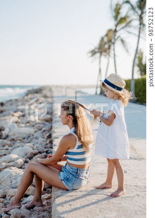 Little girl making hairstyle her mother, enjoying summer time at sea. 98752123