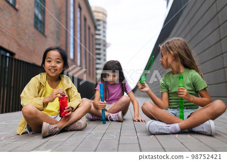 Happy three friends enjoying summer time in the city, blowing bubbles. 98752421