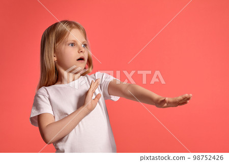 Close-up studio shot of a nice blonde little girl in a white t-shirt posing against a pink background. 98752426