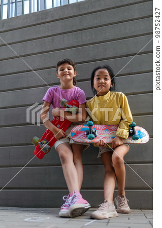Happy friends posing together in city, standing in front of concrete wall, holding skateboards and looking at camera. Happy friends posing together in city, standing in front of concrete wall, holding skateboards and looking at camera. 98752427