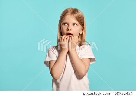 Close-up studio shot of a lovely blonde little girl in a white t-shirt posing against a blue background. Close-up studio shot of a lovely blonde little girl in a white t-shirt posing against a blue background. 98752454
