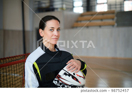 Close-up of woman floorball goalkeeper in helmet concetrating on game in gym. Close-up of woman floorball goalkeeper in helmet concetrating on game in gym. 98752457