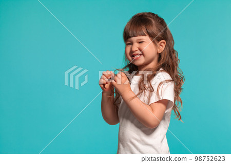 Beautiful little girl wearing in a white t-shirt is posing against a blue studio background. 98752623