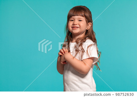 Beautiful little girl wearing in a white t-shirt is posing against a blue studio background. Beautiful little girl wearing in a white t-shirt is posing against a blue studio background. 98752630