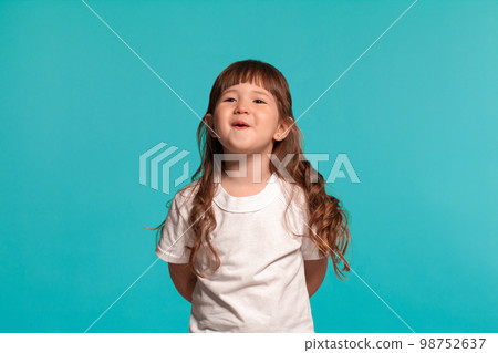 Beautiful little girl wearing in a white t-shirt is posing against a blue studio background. 98752637