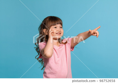 Beautiful little girl wearing in a pink t-shirt is posing against a blue studio background. 98752658