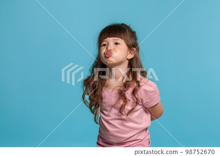 Beautiful little girl wearing in a pink t-shirt is posing against a blue studio background. 98752670
