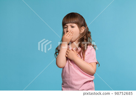 Beautiful little girl wearing in a pink t-shirt is posing against a blue studio background. 98752685