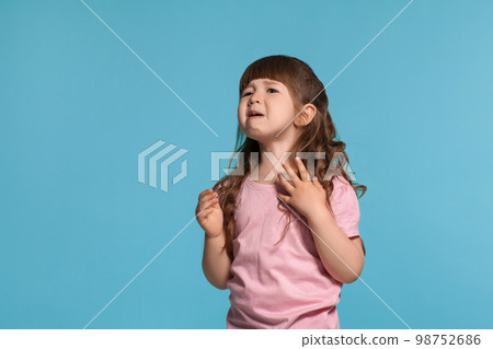 Beautiful little girl wearing in a pink t-shirt is posing against a blue studio background. Beautiful little girl wearing in a pink t-shirt is posing against a blue studio background. 98752686