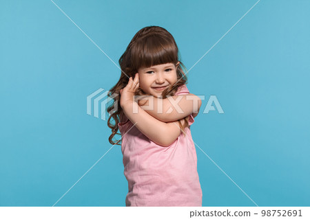 Beautiful little girl wearing in a pink t-shirt is posing against a blue studio background. 98752691