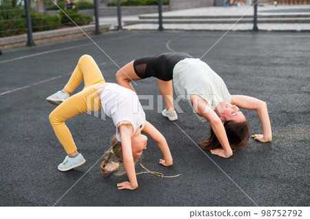 A little girl and her mom do a bridge exercise at the outdoor sports ground.  98752792