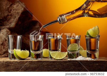 Tequila is poured from a bottle into a glass. Tequila is poured from a bottle into a glass. 98753632
