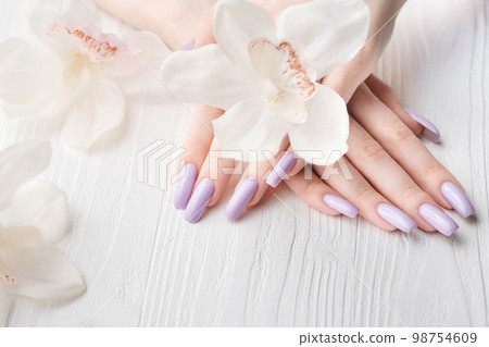 Girl's hands with delicate purple manicure and orchid flowers Girl's hands with delicate purple manicure and orchid flowers 98754609