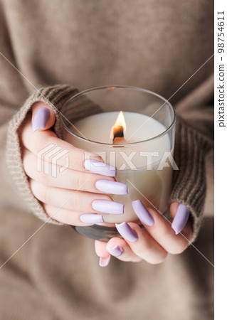 The hands of a young girl with a beautiful light purple manicure hold a candle The hands of a young girl with a beautiful light purple manicure hold a candle 98754611