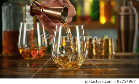 Detail of pouring whiskey into glass with ice. 98754967