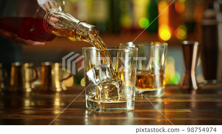 Detail of pouring whiskey into glass with ice. Detail of pouring whiskey into glass with ice. 98754974