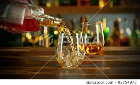 Detail of pouring whiskey into glass with ice. Detail of pouring whiskey into glass with ice. 98754976