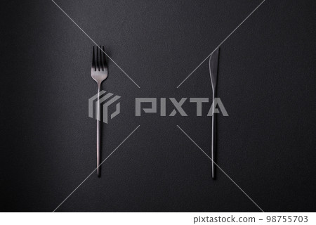 Metal kitchen knife and fork on a dark textured concrete background Metal kitchen knife and fork on a dark textured concrete background 98755703