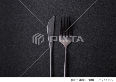 Metal kitchen knife and fork on a dark textured concrete background Metal kitchen knife and fork on a dark textured concrete background 98755709