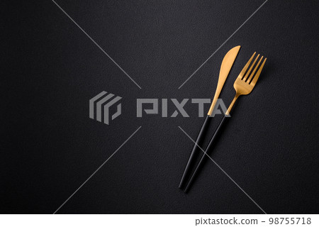 Metal kitchen knife and fork on a dark textured concrete background Metal kitchen knife and fork on a dark textured concrete background 98755718