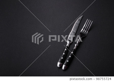 Metal kitchen knife and fork on a dark textured concrete background 98755724