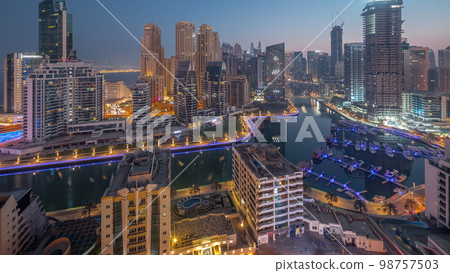 Dubai Marina with several boats and yachts parked in harbor and skyscrapers around canal aerial night to day . Dubai Marina with several boats and yachts parked in harbor and skyscrapers around canal aerial night to day . 98757503