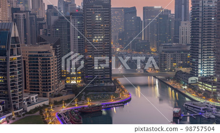 Dubai Marina with several boats and yachts parked in harbor and skyscrapers around canal aerial night to day . Dubai Marina with several boats and yachts parked in harbor and skyscrapers around canal aerial night to day . 98757504
