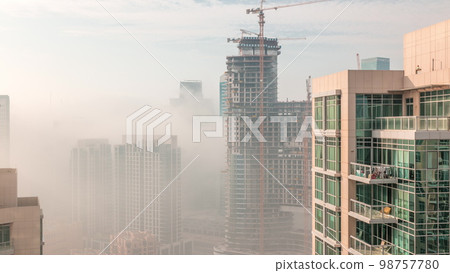 Dubai skyscrapers covered by morning fog in business bay district during sunrise . 98757780
