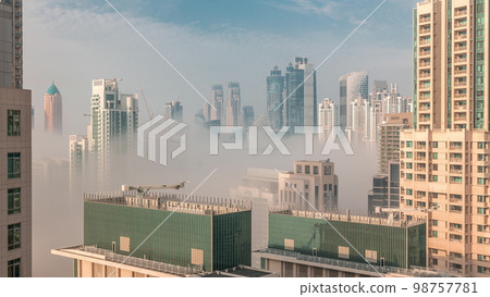 Dubai skyscrapers covered by morning fog in business bay district during sunrise . 98757781