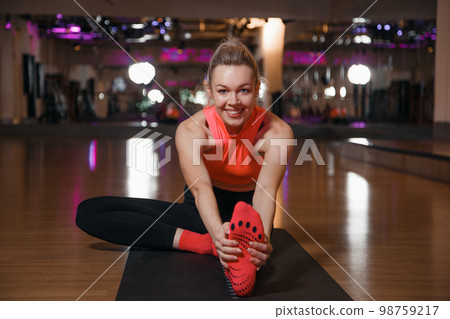 Young attractive woman practicing yoga. Woman sitting in seated forward bend position. Dedicated to fitness. Beautiful young woman in sportswear doing stretching while sitting on the floor in gym. 98759217