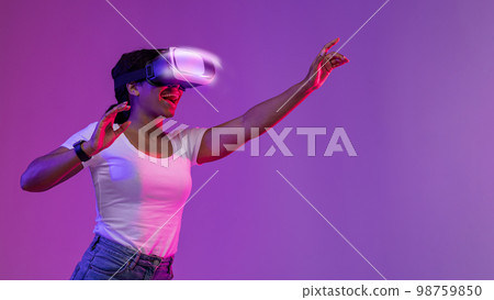 Excited Black Woman Wearing VR Headset Experiencing Virtual Reality In Neon Light Excited Black Woman Wearing VR Headset Experiencing Virtual Reality In Neon Light 98759850