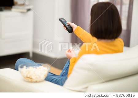 Unrecognizable brunette woman switching channels on TV Unrecognizable brunette woman switching channels on TV 98760019