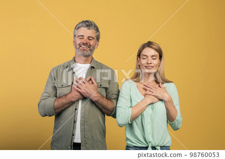 Thank you. Grateful middle aged couple with closed eyes keeping both hands on chest, expressing grattitude and kindness 98760053