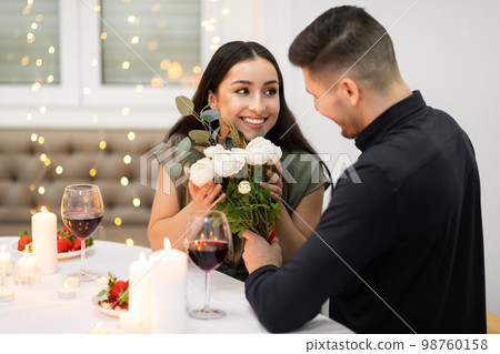 Happy attractive woman holding flowers, looking at her handsome boyfriend 98760158