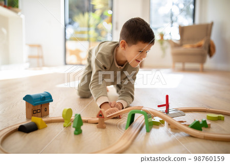 Glad cheerful small european boy in pajamas on floor plays with road and cars alone, enjoy fantasy at spare time 98760159
