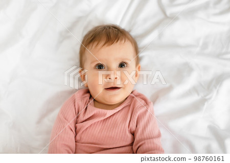 Closeup shot of pretty little girl resting on bed and smiling, relaxing at home on white linens, top view 98760161