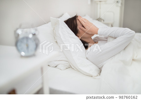 Exhausted woman lying in bed, touching her face 98760162