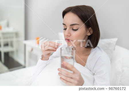 Young woman holding glass of water and pink madicine Young woman holding glass of water and pink madicine 98760172