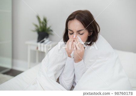 Sick young lady sneezing, staying in bed at home 98760178