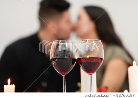 Selective focus on glasses with red wine over kissing couple 98760197