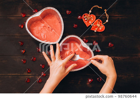 Woman removes dough from spoon with her finger, process of making cake in form of heart. 98760644
