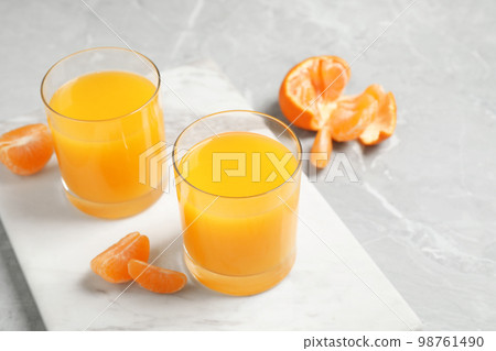 Glasses of fresh tangerine juice and fruits on light table Glasses of fresh tangerine juice and fruits on light table 98761490