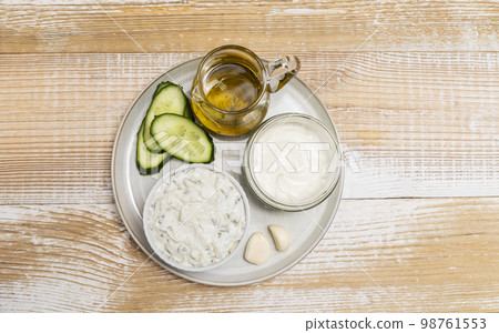 traditional greek yogurt sauce Tzatziki,dressing in white bowl, made of grated cucumbers, sour cream yogurt,olive oil,garlic,herbs with ingredients on wooden table. Top view, horizontal, copyspace 98761553