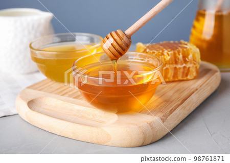 Dripping tasty aromatic honey from dipper into bowl on light grey table 98761871