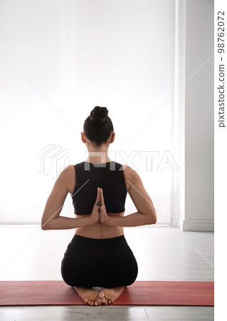 Woman practicing vajrasana with namaste behind back in yoga studio 98762072