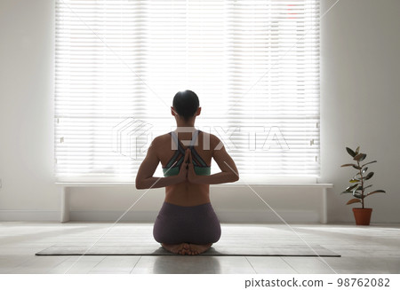 Woman practicing vajrasana with namaste behind back in yoga studio 98762082