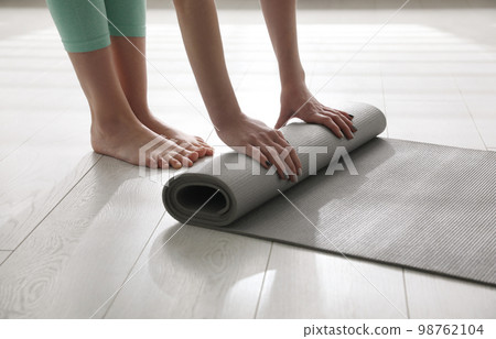 Woman rolling her mat on floor in yoga studio, closeup Woman rolling her mat on floor in yoga studio, closeup 98762104