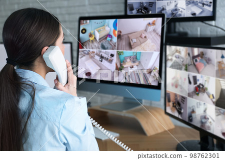 Female security guard talking by telephone near monitors at workplace Female security guard talking by telephone near monitors at workplace 98762301