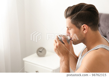 Man with cup of coffee in bedroom. Lazy morning 98762315